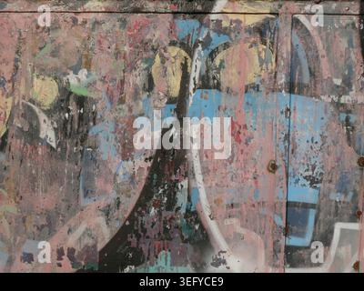 Weathered street art on a metal cabinet shows flaking blue and pink paint layers, rusted screws, and scratches, forming a gritty urban decay texture i Stock Photo
