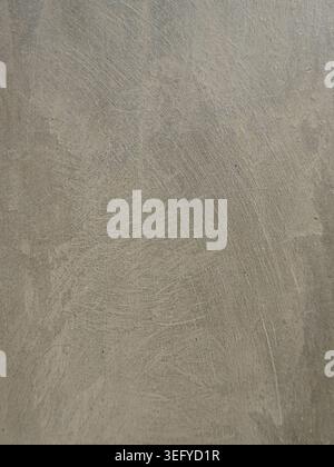 Close-up of a weathered concrete wall with gritty, grainy texture, scratched plaster marks, and mottled gray taupe tones, forming a neutral grunge bac Stock Photo