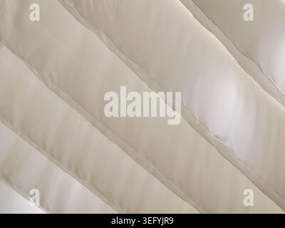 A detailed macro shot of cream-colored quilted fabric. Diagonal lines of stitching create a raised pattern with a soft, inviting texture. The neutral Stock Photo