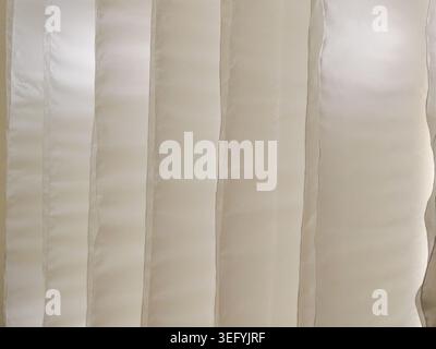 Close-up view of vertical beige blinds. Natural light filters through the panels, creating subtle shadows and highlighting the texture of the material Stock Photo