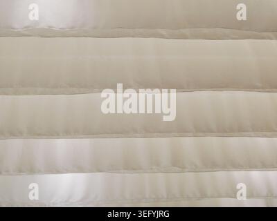 A close-up, abstract view of horizontal blinds in a textured beige material. Subtle sparkles are visible, with sunlight filtering through the slats, c Stock Photo