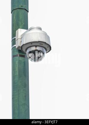 A close-up shot of a modern outdoor security surveillance camera mounted on a textured green pole. The camera features a dome lens and is set against Stock Photo