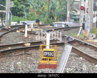 Close-up view of railway tracks converging at a junction, featuring a yellow signal box and a red signal light. Daytime scene with foliage in the back Stock Photo