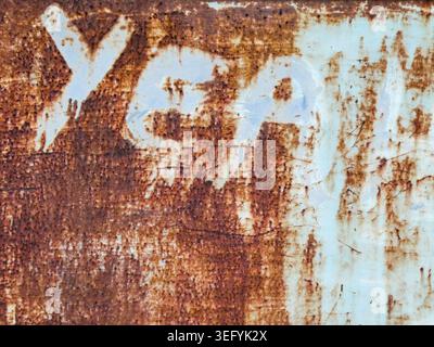 Close-up of a weathered rusted metal surface with peeling pale blue paint and bold graffiti letters, revealing gritty texture, corrosion, and an urban Stock Photo