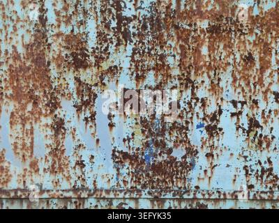 Close up of weathered blue metal panel showing orange rust patches and peeling paint, creating a gritty grunge texture with irregular patterns and ind Stock Photo