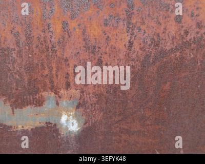 Close-up of a weathered rusted metal surface featuring orange-brown patina, pale green streaks, and a white patch, conveying rugged industrial texture Stock Photo
