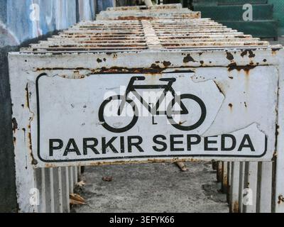 Rusted white bicycle parking sign with a black bike icon on a weathered concrete staircase, framed by green and blue railing, conveying an urban, aged Stock Photo