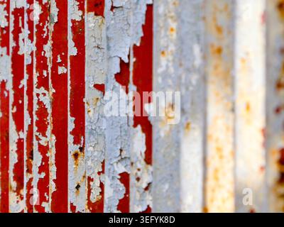 Macro view of a rusted corrugated metal surface with peeling white paint revealing red underneath. The textured, aged material shows signs of weatheri Stock Photo