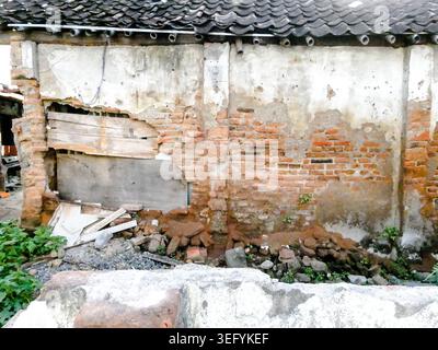 A close view of a damaged brick wall with peeling plaster, showing structural decay and masonry textures of an old traditional building in Indonesia Stock Photo