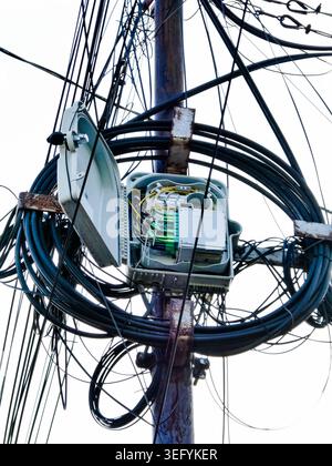 An open fiber optic distribution box attached to a utility pole in Yogyakarta, Indonesia, showing tangled black cables and internal green wiring Stock Photo