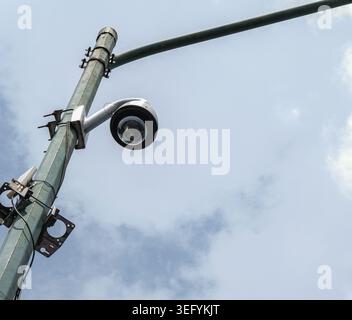 a cctv surveillance camera mounted on a tall metal utility pole, captured from an upward angle against a cloudy sky in yogyakarta, indonesia. the imag Stock Photo