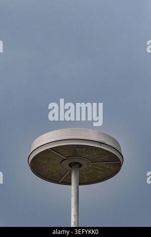 Low angle vertical shot of a circular modern street lamp post set against an expansive clear blue sky, showcasing industrial design, clean geometry, a Stock Photo