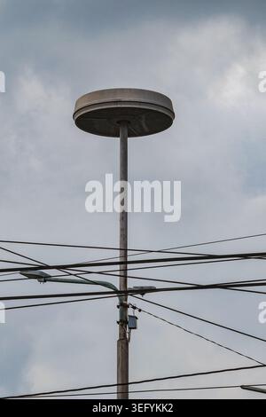 A close-up shot of a unique circular streetlight mounted on a pole with numerous power cables running across the frame under a cloudy sky in Yogyakart Stock Photo