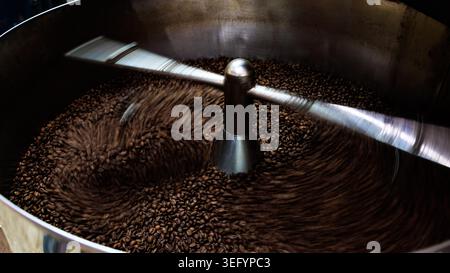 Closeup of an industrial coffee roaster cooling tray with mechanical arms stirring freshly roasted coffee beans during production. Stock Photo