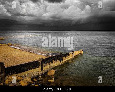 dark and stormy black clouds in the distance over the sea on a coastal estuary.  A storm is gathering on the horizon. Stock Photo