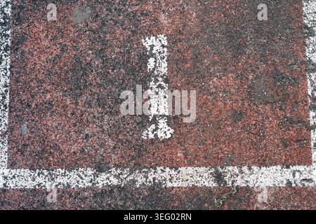 A faded and scratched white number 1 inside a painted frame on an old textured outdoor athletics track, representing leadership, first place, or begin Stock Photo