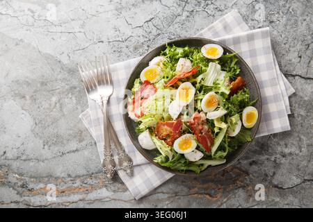 Keto salad with boiled quail eggs, bacon, mozzarella, and mixed lettuce, close-up on a plate on a table. Horizontal top view from above Stock Photo