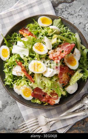 crispy, delicious salad of soft-boiled quail eggs, bacon, mozzarella, sesame seeds, and mixed greens, close-up on a plate on the table. Vertical top v Stock Photo