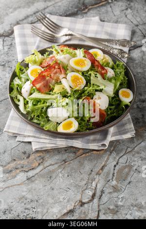 Fresh salad of frisee lettuce, mozzarella cheese balls, halved boiled quail eggs, crispy bacon and sesame seeds closeup on the plate on the table. Ver Stock Photo