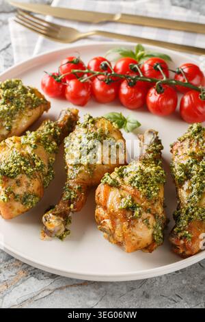 Baked pesto chicken drumsticks with cherry tomatoes closeup on the plate on the table. Vertical Stock Photo