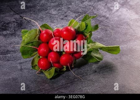 Vibrant red radishes with fresh green leaves arranged on dark textured background. Studio shot, bright lighting highlights crisp texture. Healthy food Stock Photo