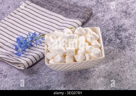 Sweet white mini marshmallows fill decorative bowl, set beside striped kitchen towel delicate blue flowers. Light grey textured background provides cl Stock Photo