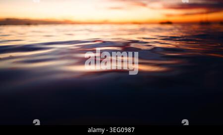 Reflecting vibrant sunset hues on ocean surface creating ripple patterns at dusk Stock Photo
