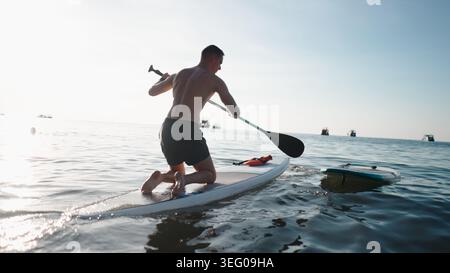 Young man paddling stand up board on ocean water at sunrise or sunset Stock Photo