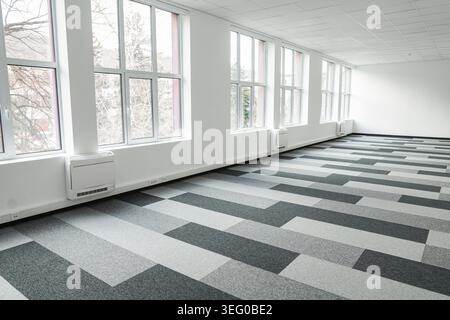 Empty office space with a checkered floor and large windows letting in natural light. The space appears spacious and bright, with no furniture in sight. The checkered floor adds a classic touch to the space design, while the large windows offer a view of t Stock Photo