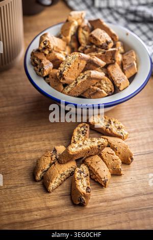 Homemade Italian biscotti cantuccini piled in an enamel bowl and scattered on a rustic wooden table, ideal for coffee or tea breaks. Warm, crunchy golden baked cookies that evoke cozy mornings and casual hospitality. Stock Photo