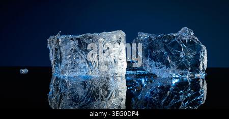 Broken ice with blue backlight on a black reflective background. Copy space. Stock Photo