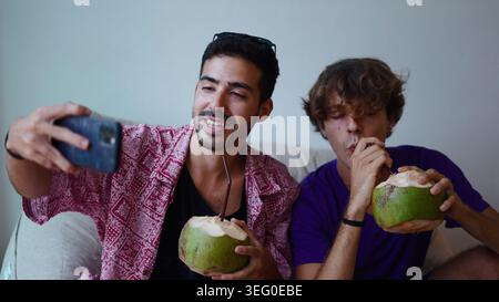 Two young men taking selfie enjoying fresh coconut drink together Stock Photo