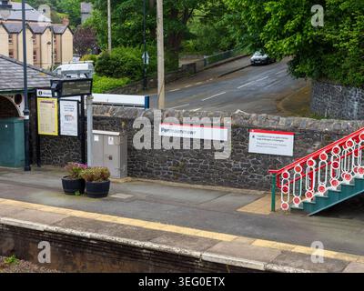 Penmaenmawr, Wales, UK, 16 May 2026: Penmaenmawr railway station platform with a stone wall, stairs, and passenger information signs on a cloudy day i Stock Photo