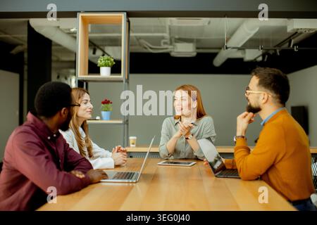 A group of professionals gathers around a wooden table, exchanging ideas and collaborating in a bright, contemporary office environment. Stock Photo