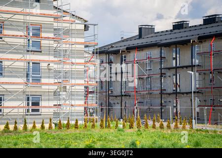 Construction site of multiple residential apartment buildings with exterior scaffolding systems for facade insulation and modern dark roofs in a subur Stock Photo