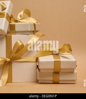 A stack of cream-colored gift boxes tied with gold satin ribbons and bows on a beige background. Stock Photo