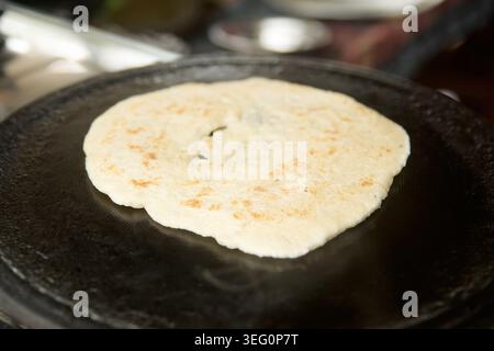 round flatbread roti with toasted brown spots, cooking dough on flat black cast iron griddle tawa pan, closeup with soft focus, south asian cuisine Stock Photo