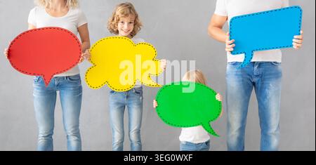 Happy family - father, mother, daughter and son - holding colorful paper speech bubble blank. People with two kids having fun indoor. Stock Photo