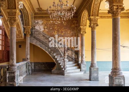 Elegant interior of a historic building in Havana, Cuba. The scene features a lavish marble staircase with iron railings, ornate columns, and yellow w Stock Photo
