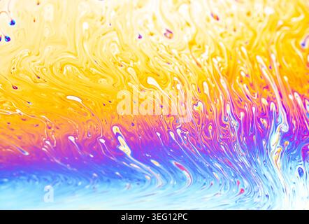 Close-up view of a soap bubble's surface displaying vibrant, swirling patterns of yellow, orange, purple, and blue Stock Photo