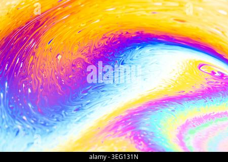 Close-up view of iridescent soap film showing interference patterns and fluid dynamics in vivid hues of yellow, blue, and purple Stock Photo