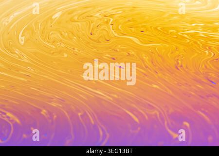 Close-up view of iridescent soap film with vibrant yellow and purple hues creating mesmerizing fluid dynamics and swirling textures Stock Photo