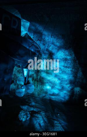 Suspended fishing boat installation inside an underground tunnel in Pula Croatia illuminated by dramatic blue lighting reflecting on rocky walls and d Stock Photo