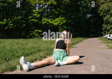 Young Woman Stretching Legs on Asphalt Before Running in Sunny Park. Stock Photo
