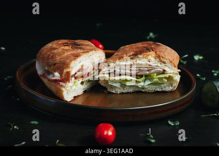 Delicious sandwich cut in half on wooden plate, surrounded by fresh ingredients Stock Photo