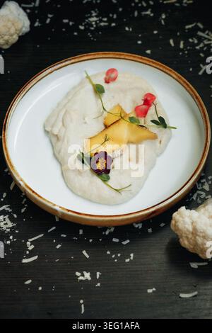 Cauliflower puree garnished with edible flowers and mango on rustic plate Stock Photo