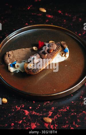 Chocolate eclair with toppings, served on a dark plate Stock Photo