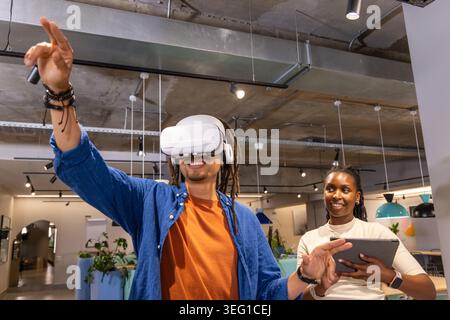 African American coworkers demonstrating VR visor in open office, man standing near center reaching Stock Photo