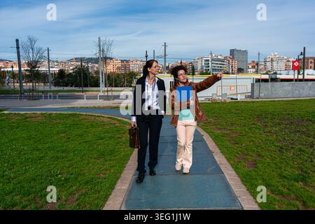 Businesswomen discussing urban development walking outdoors in city park Stock Photo