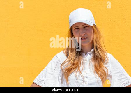 Woman wearing white baseball cap on bright yellow background Stock Photo